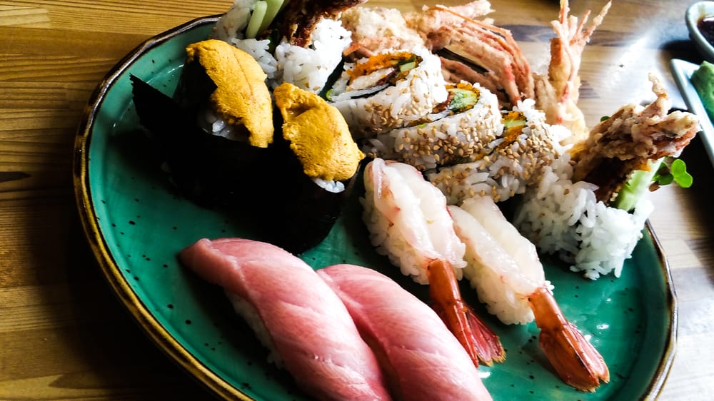 Uni, toro, shrimp and rolls on a green ceramic plate